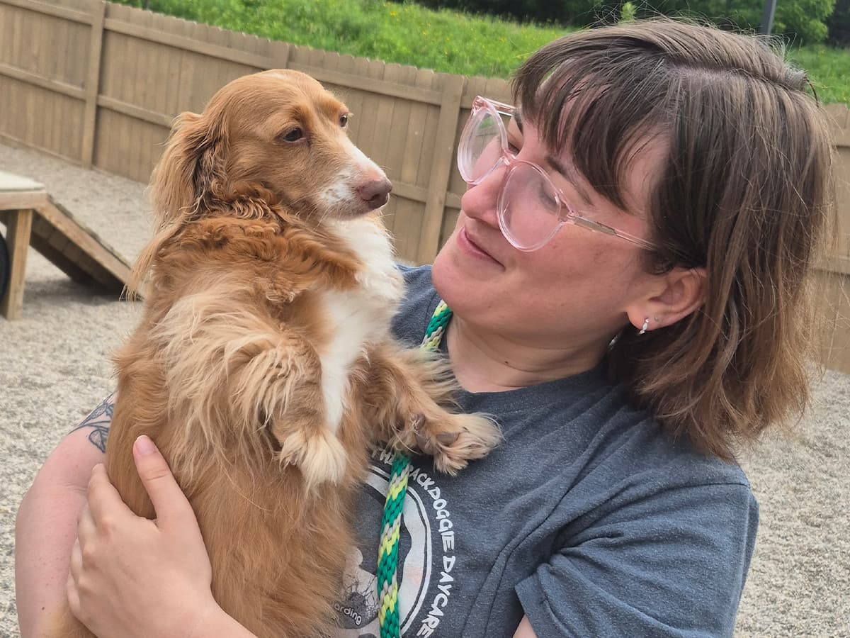 Handler holding a dog in the outdoor play yard at Leader of the Pack