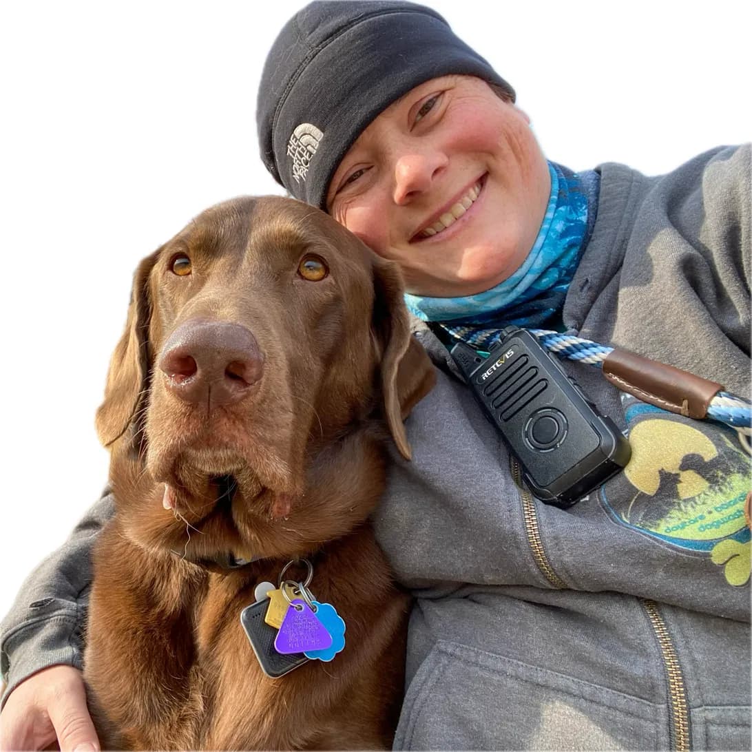 Mary cheek-to-cheek with a chocolate Lab, radio clipped to her jacket, on shift at Leader of the Pack