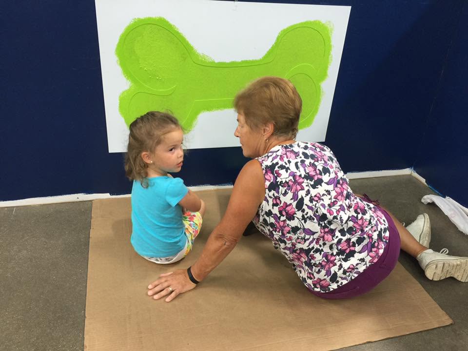 Marion and a young Emma sitting on the floor painting a large green bone on the wall