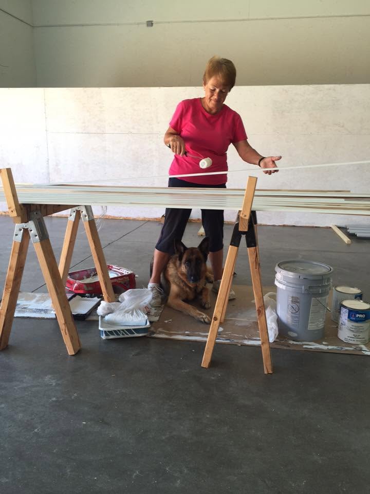 Marion painting long trim boards on sawhorses while a dog lies underneath